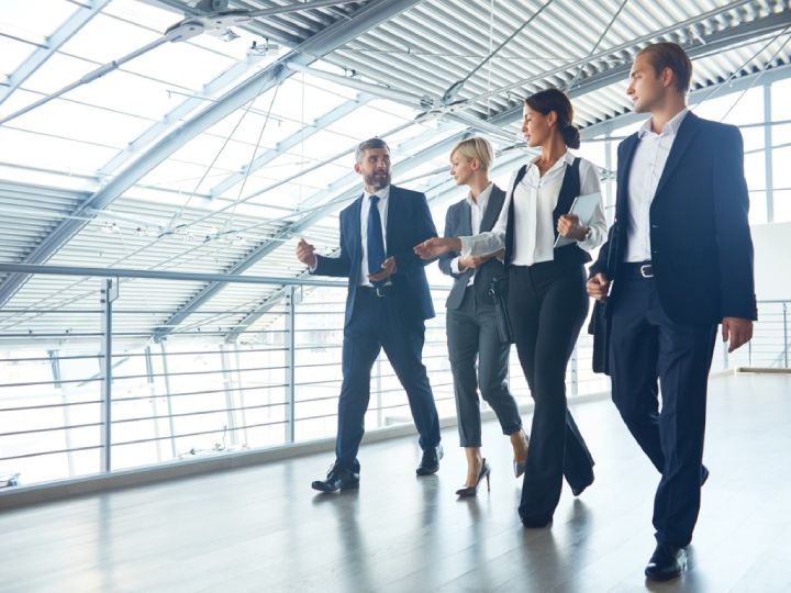 A group of confident corporate professionals walking in a modern office, representing the benefits of American accent training for clarity and career success