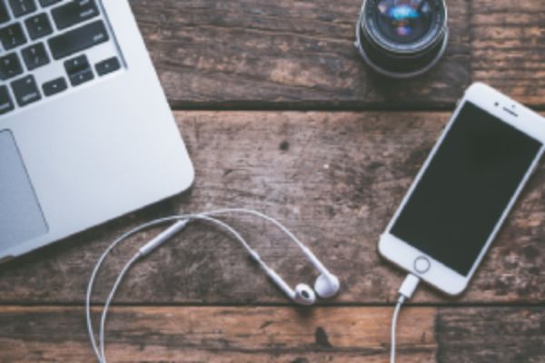 Laptop, smartphone, and headphones on a wooden desk, representing flexible American accent training available on any device